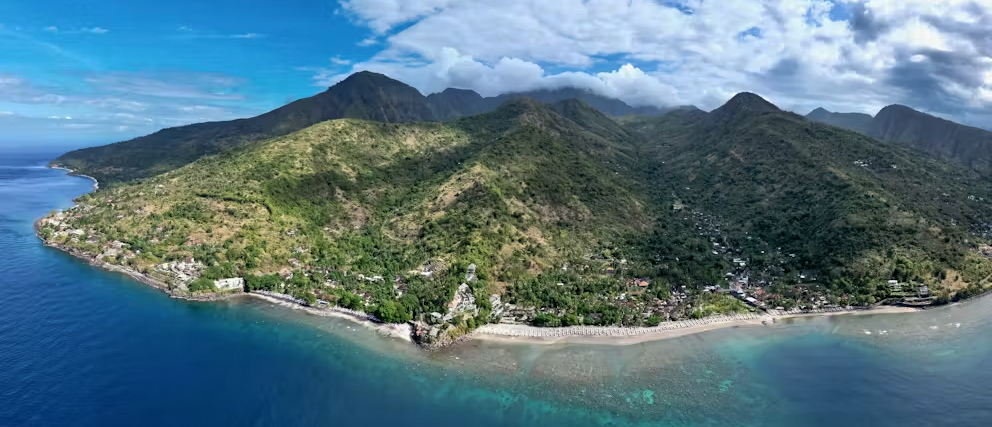 Stunning aerial view of Amed, Bali, showing the coast, turquoise ocean, and majestic mountains.