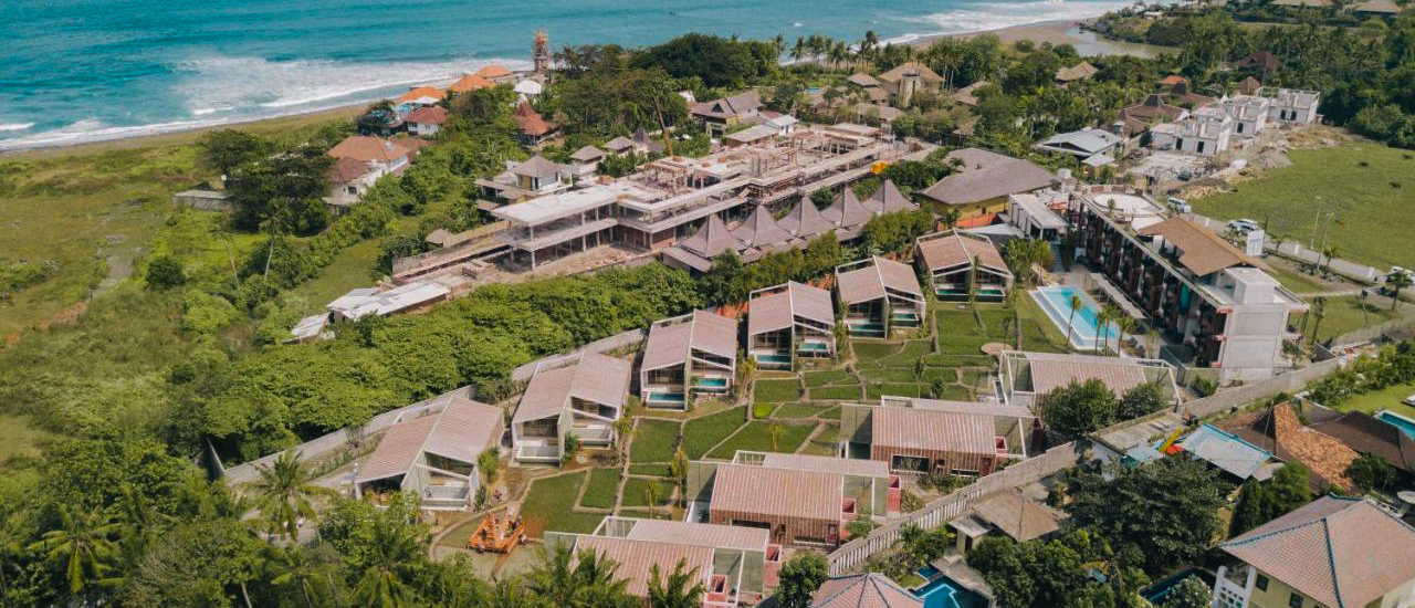 Aerial view of modern resort villas and buildings along the green coastline of Canggu, Bali.