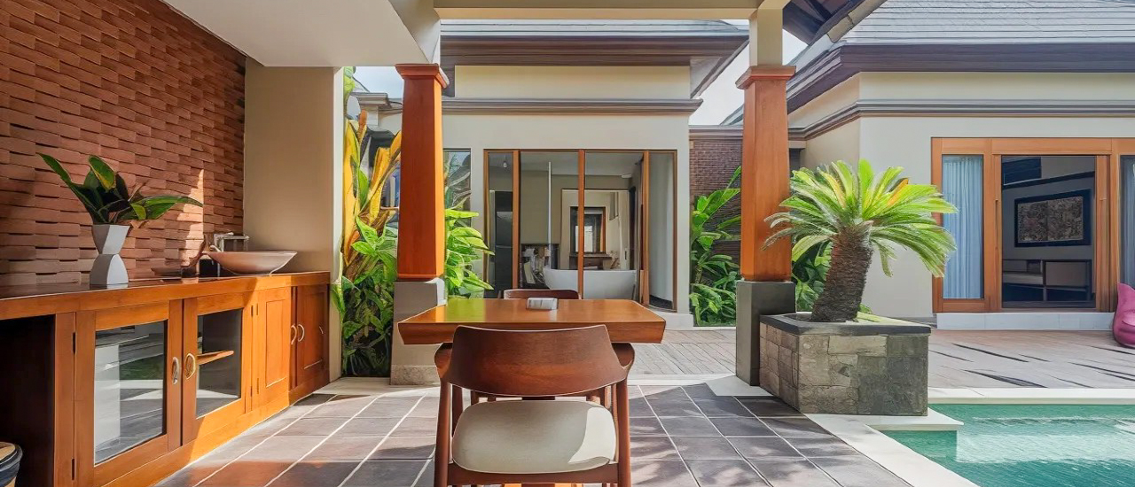A luxurious resort patio in Bali with a dining table, tropical plants, and a private pool.