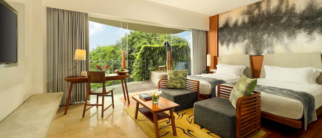 Luxurious hotel room in Sanur with two beds, sitting area, and balcony with tropical views.