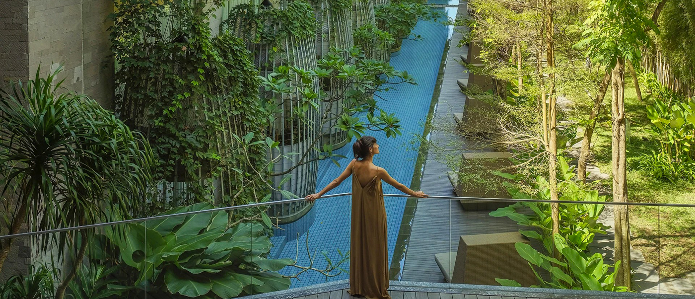 Woman in a brown dress enjoying the lush green views and long pool at a resort in Sanur.