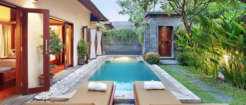 Luxurious private pool villa in Seminyak, Bali, with lounge chairs and lush tropical garden.