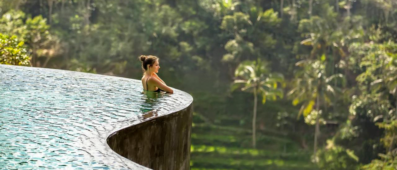 Woman relaxing in an infinity pool overlooking a lush green jungle in Ubud, Bali.