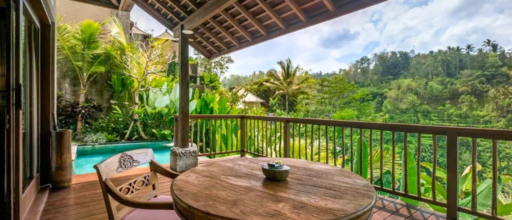 A private balcony with a wooden table, a small pool, and a lush jungle view in Ubud.