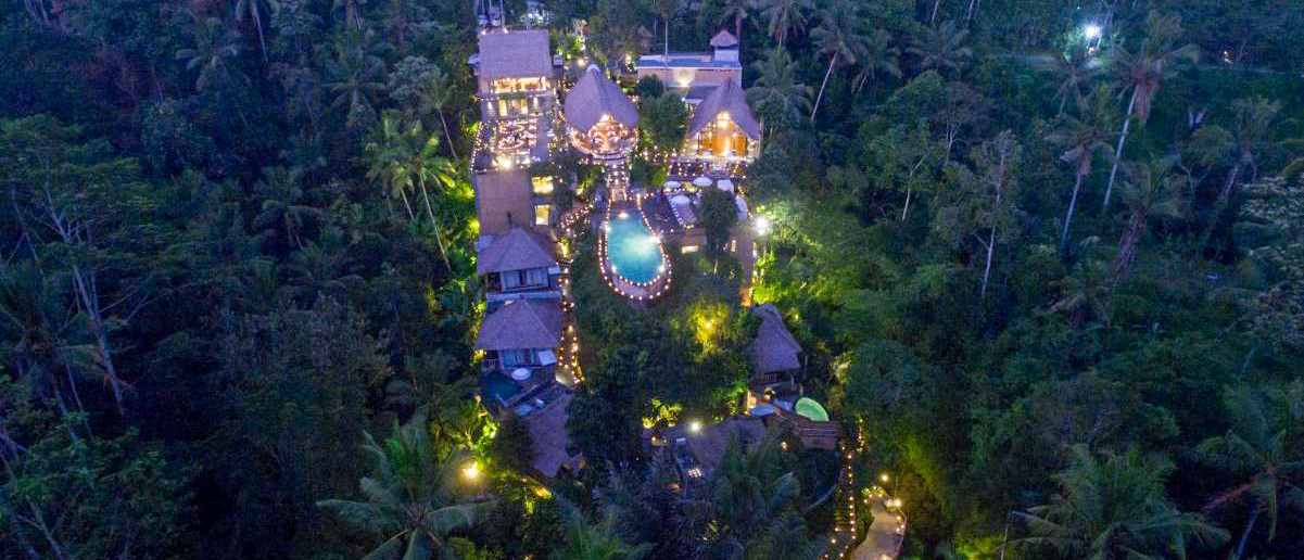 An aerial view of the illuminated Kayon Resort in Ubud, nestled within a lush tropical jungle.