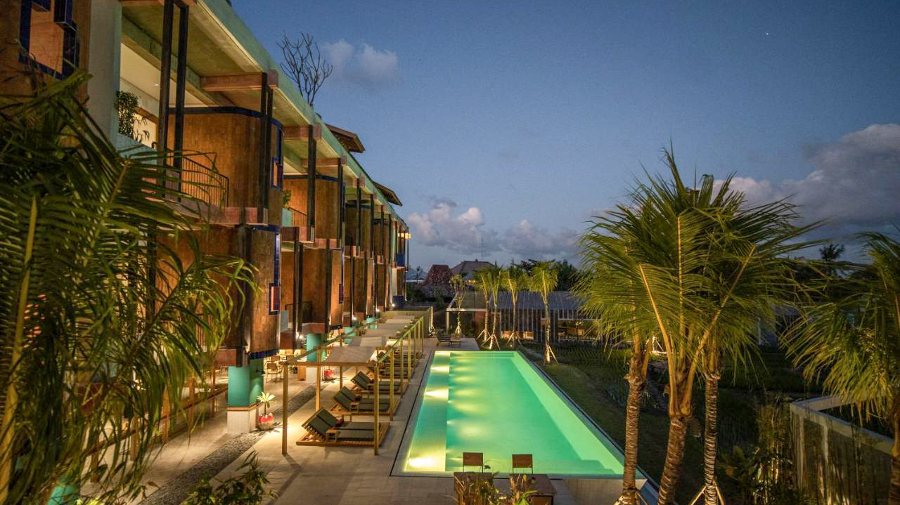 A luxurious resort with a long, illuminated swimming pool and palm trees at twilight in Canggu, Bali.