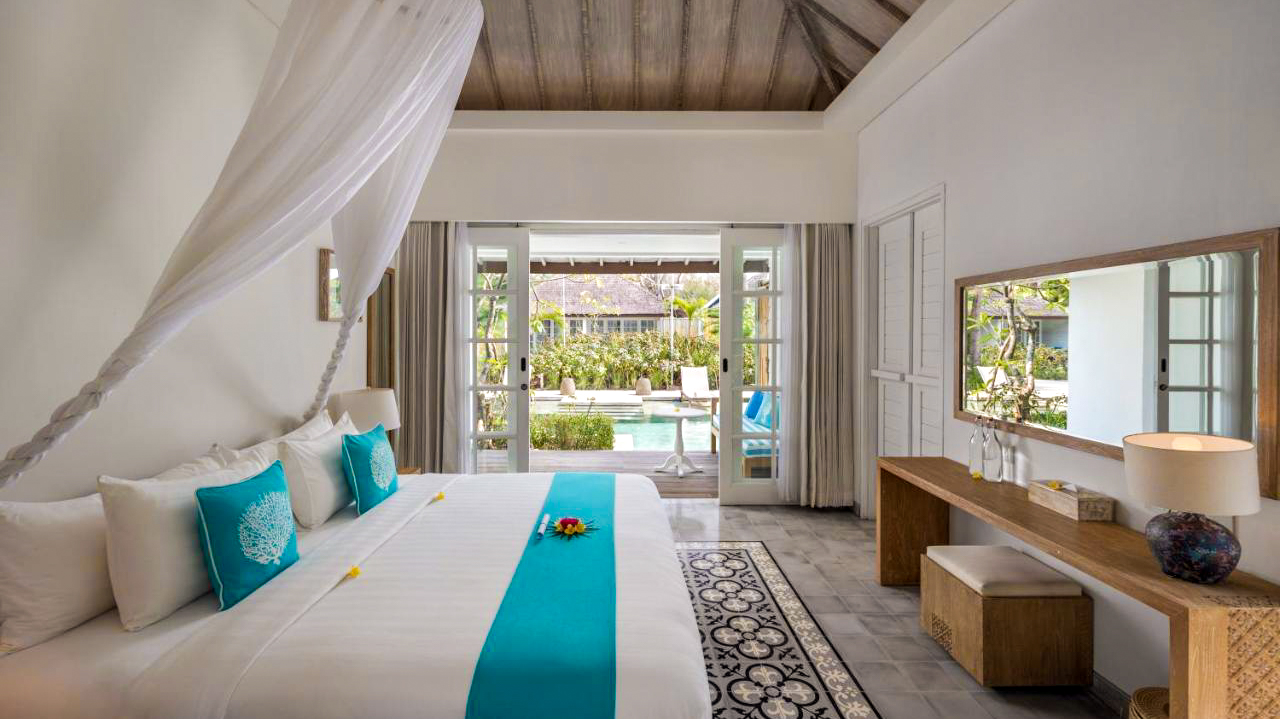 Beautiful Bali resort bedroom with a canopy bed and French doors opening to a lush pool area.