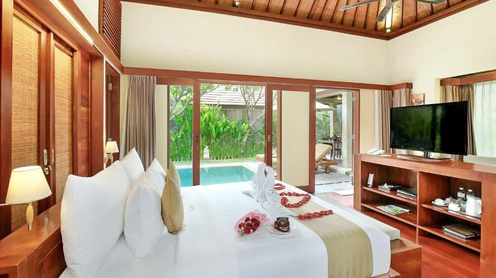 Luxurious Balinese villa bedroom with a king-size bed, swan towels, and private pool view.