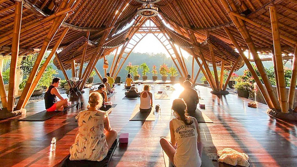 Guests practice yoga in a beautiful open-air bamboo studio overlooking the lush Ubud jungle.