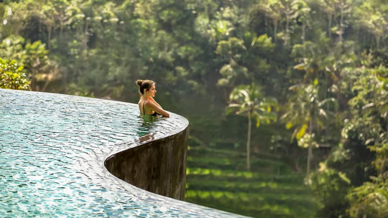 Relaxing woman in an infinity pool with stunning views of the tropical Ubud jungle.