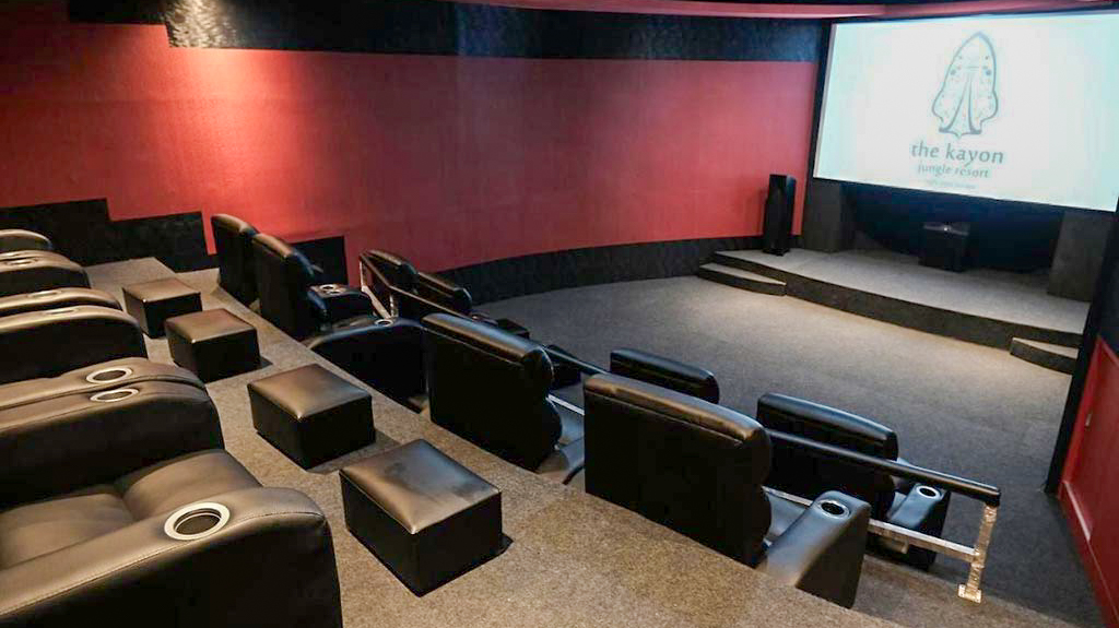 A luxurious private cinema with comfortable black recliners and a large screen displaying the resort logo.