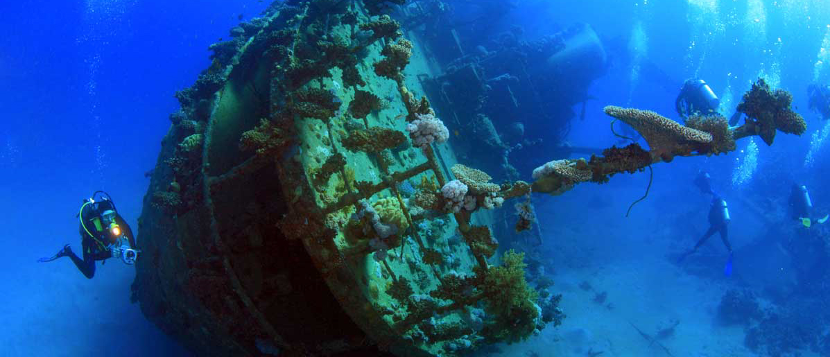 Scuba divers explore the coral-covered USS Liberty shipwreck in the clear blue waters of Amed, Bali.