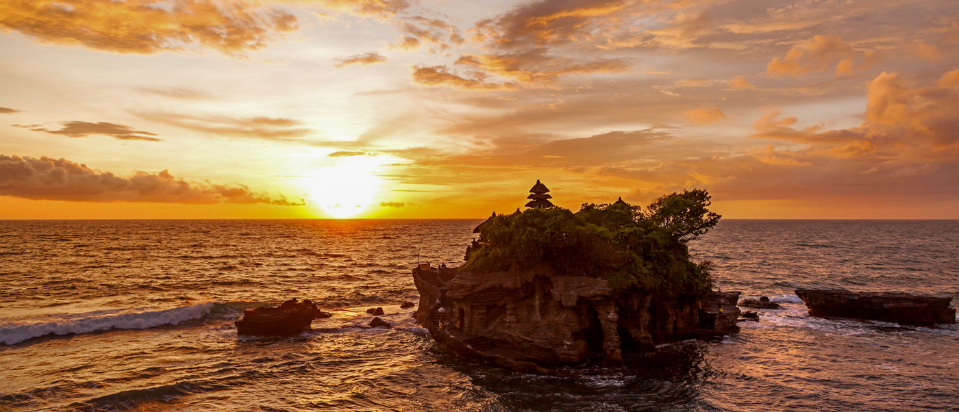 Breathtaking sunset over the sea at Tanah Lot Temple, with warm orange sky and gentle waves.
