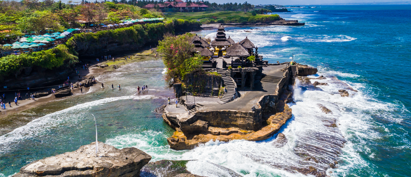 Breathtaking Tanah Lot temple on a rocky island, with waves crashing and people exploring the Bali coastline.