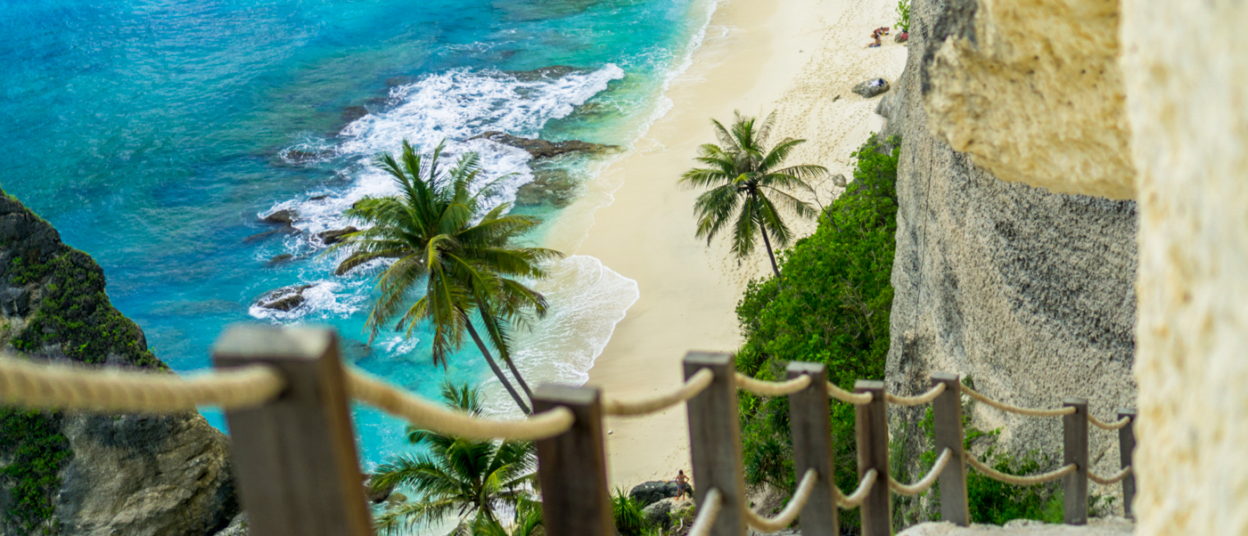 View from a cliff path overlooking a beautiful white sand beach in Bali with turquoise water.