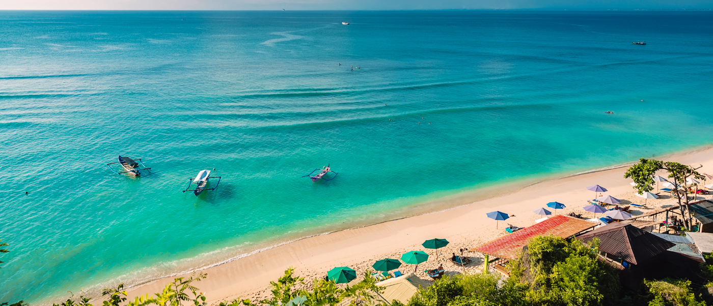 Beautiful Lovina Beach in Bali with clear turquoise water, small boats, and beach umbrellas.