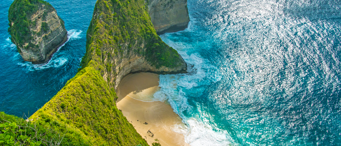 Aerial view of a dramatic coastline with lush green cliffs, a secluded beach, and turquoise ocean.