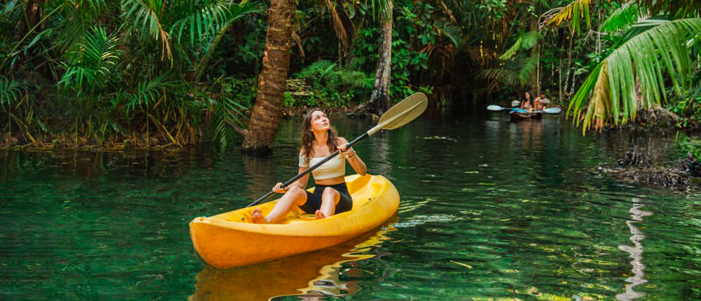 Young woman paddling a yellow kayak through serene Nusa Lembongan mangroves, enjoying the lush scenery.
