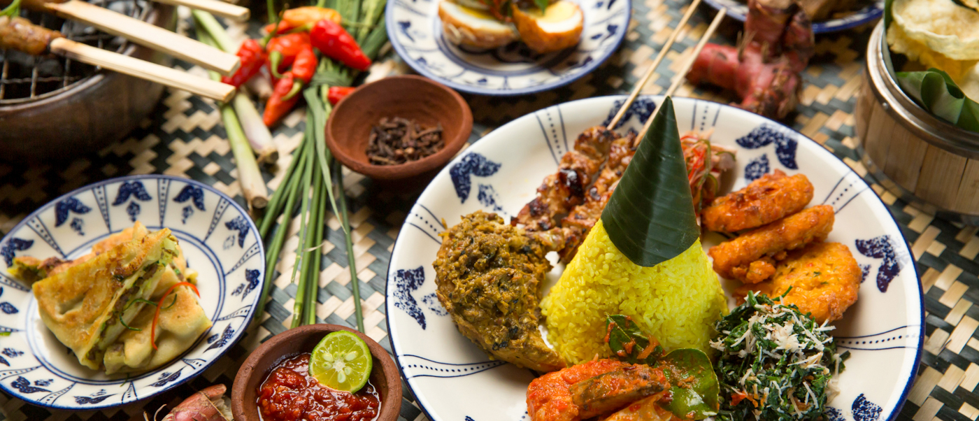 A vibrant spread of traditional Balinese dishes, including yellow cone rice and satay, served in Ubud.