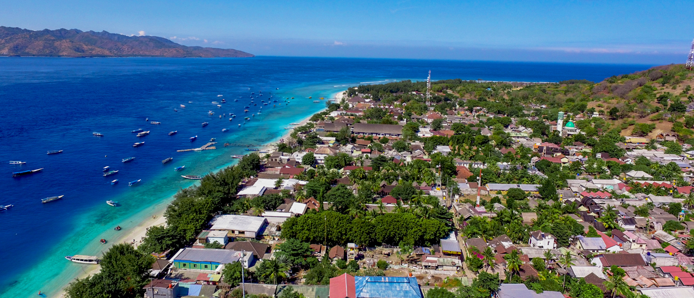 Gili Trawangan's stunning coastline with turquoise waters, numerous boats, and a lively village under a clear sky.
