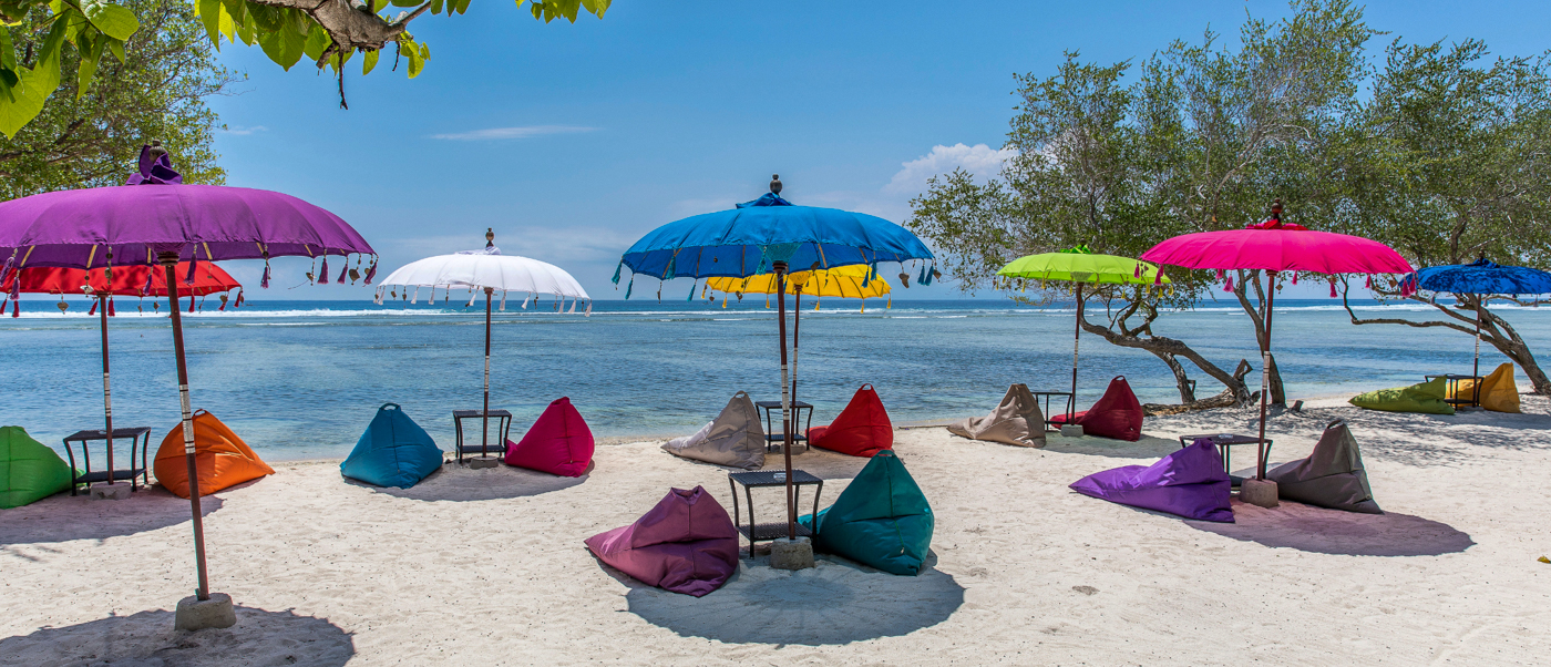 Colorful umbrellas and beanbag chairs line a pristine white sand beach on Gili Trawangan.