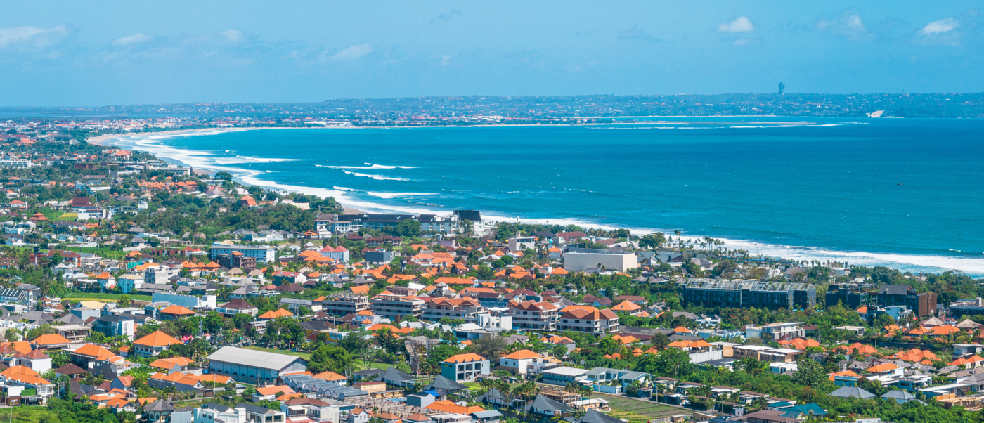 Panoramic view of Seminyak Beach, showing the town's orange roofs along the blue ocean.