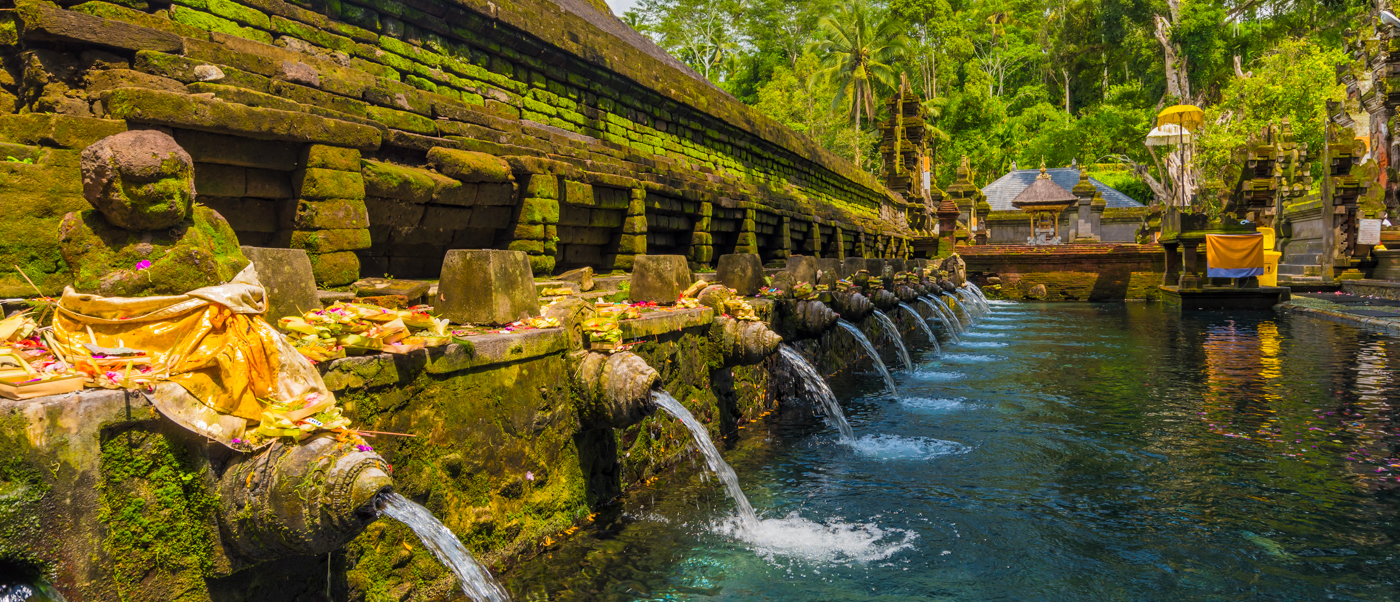 Sacred water flows from moss-covered stone spouts into a serene purification pool at Tirta Empul temple.