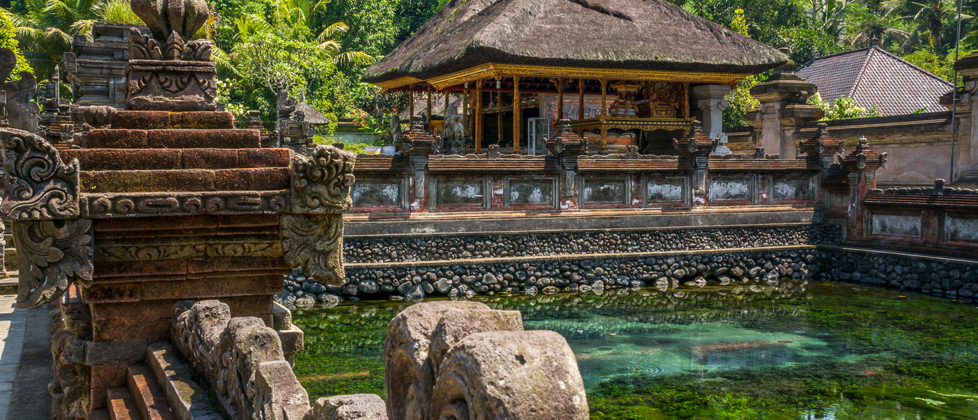 Intricate stone architecture surrounds a clear sacred spring at Tirta Empul temple in Bali.