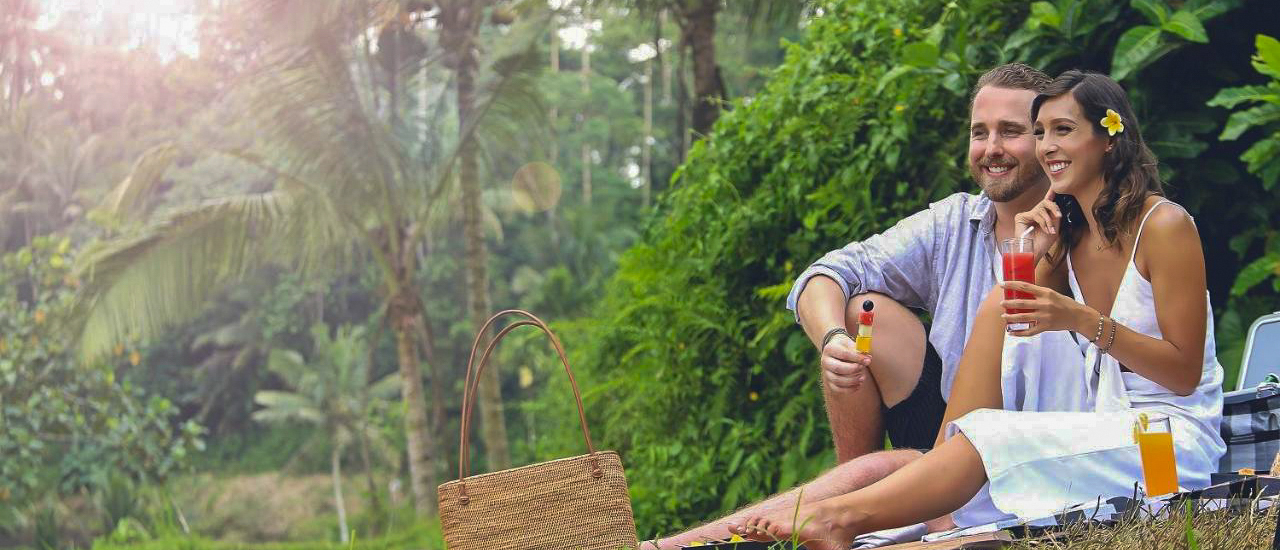 Smiling couple enjoying a picnic lunch with tropical drinks amidst lush green scenery in Ubud.