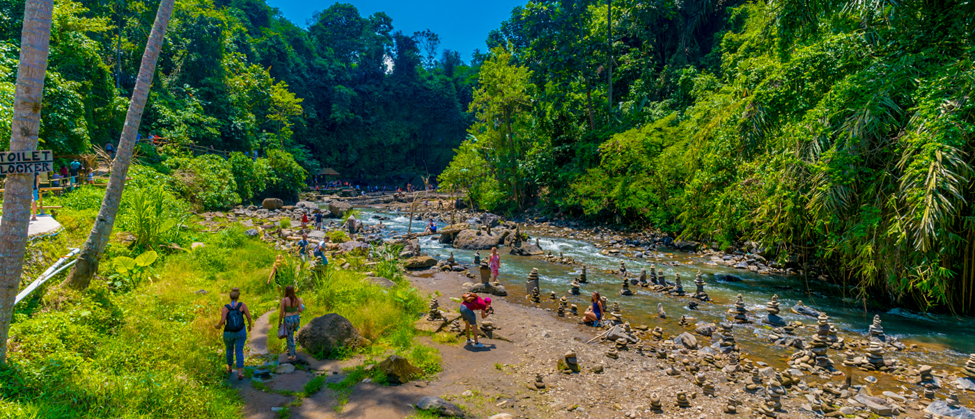 Tourists explore the rocky riverbed and lush jungle surroundings at Tegenungan Waterfall in Bali.