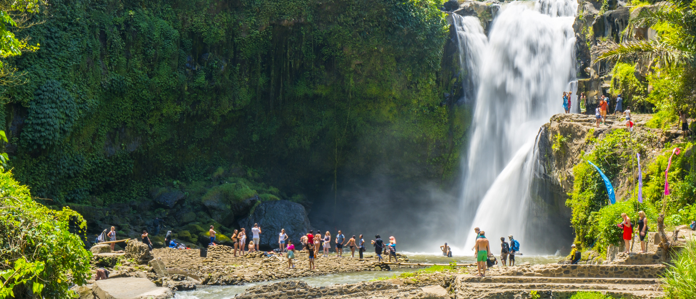 Tourists gather at the base of the majestic Tegenungan Waterfall in Bali, surrounded by lush jungle.