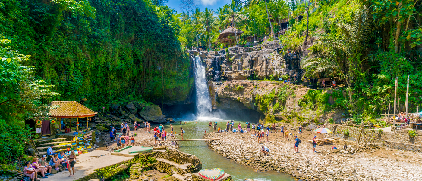 Tourists enjoy swimming and relaxing at the majestic Tegenungan Waterfall surrounded by lush jungle in Bali.