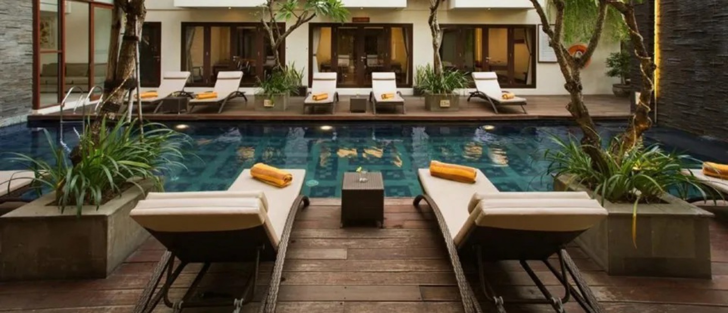 Serene hotel swimming pool in Seminyak, Bali, surrounded by lounge chairs and lush greenery.