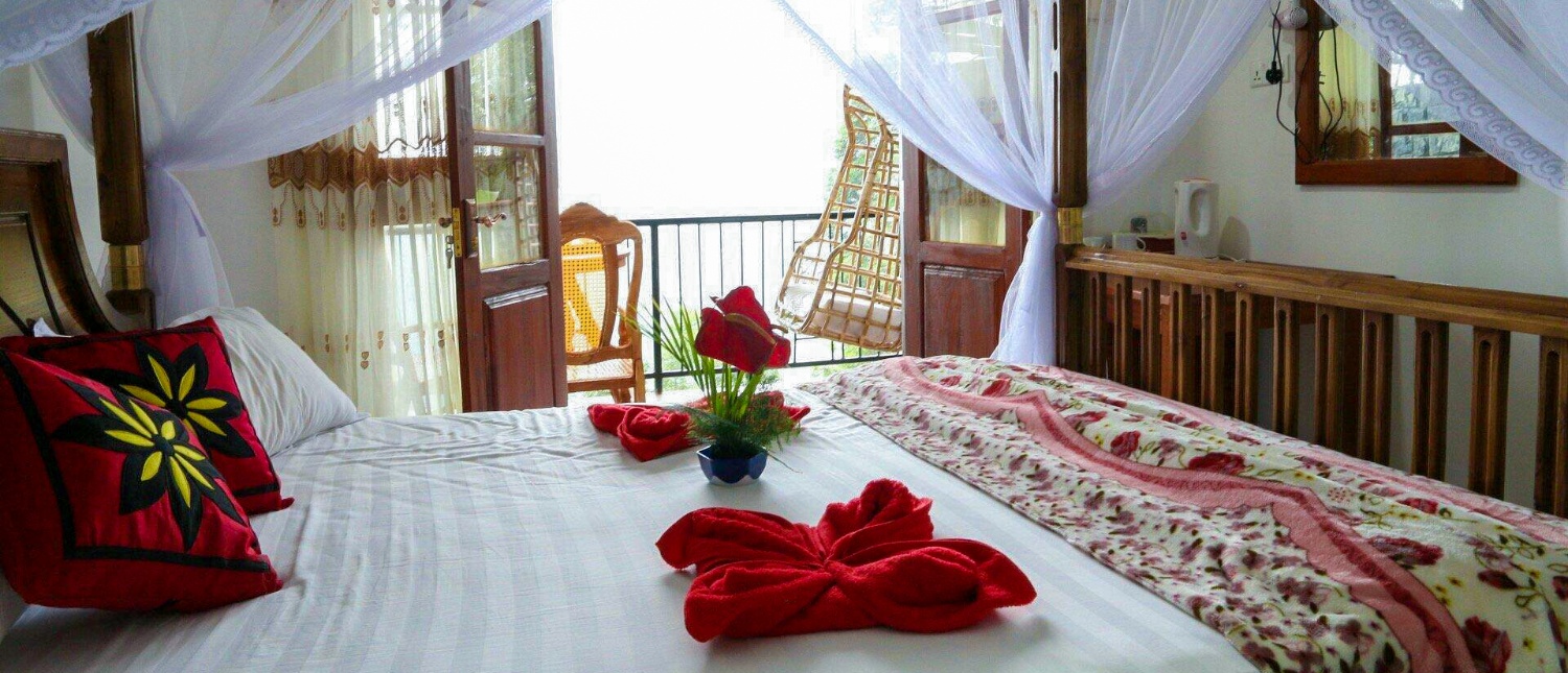 A romantic four-poster bed with red floral decor and a balcony view of misty hills in Ella.