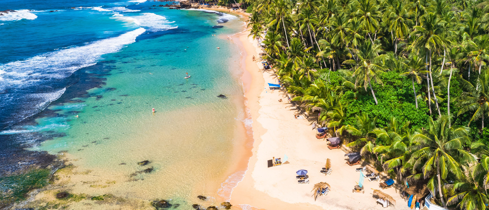 People relaxing on the vibrant Weligama beach with clear turquoise waters and swaying palm trees.