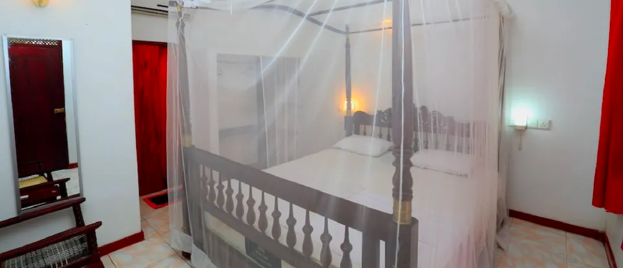 An inviting bedroom with a dark wood four-poster bed, white mosquito net, and warm lighting.