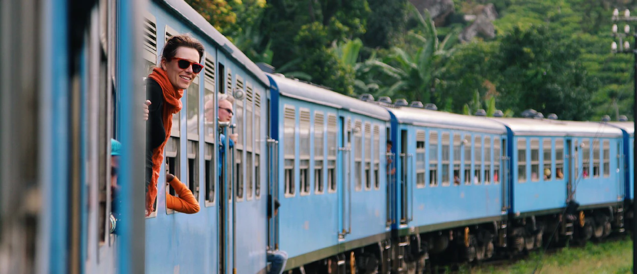 A smiling traveler leans from a blue train window, enjoying the scenic highland journey in Sri Lanka.