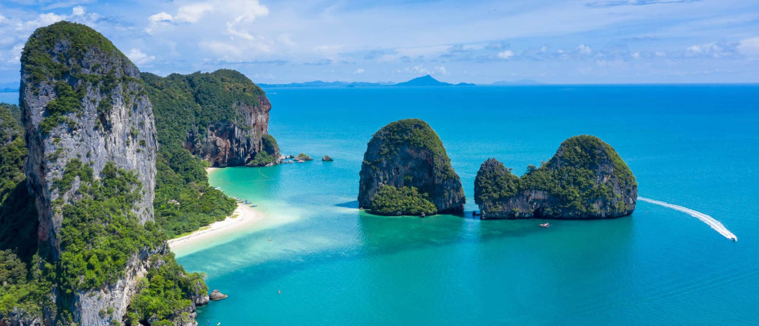 Krabi's stunning tropical coastline with towering limestone karsts, a white beach, turquoise sea, and a boat.