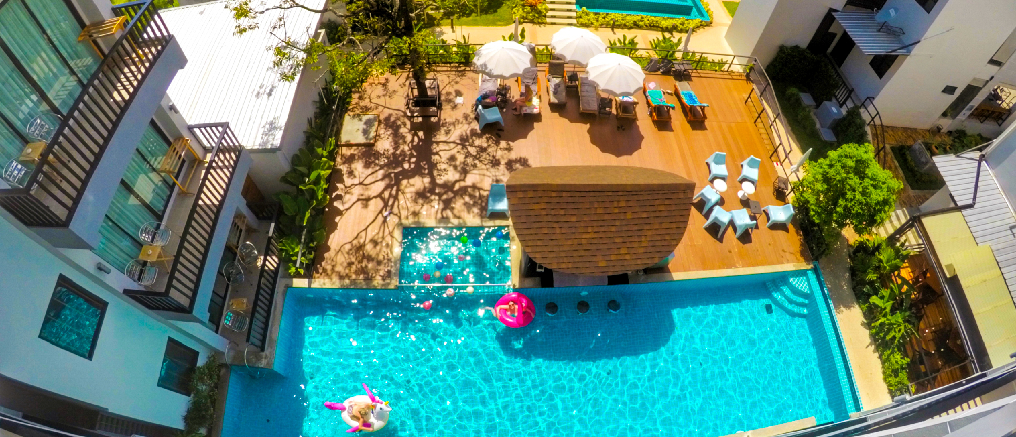 Aerial view of a vibrant resort pool in Krabi with people relaxing on floats and umbrellas.