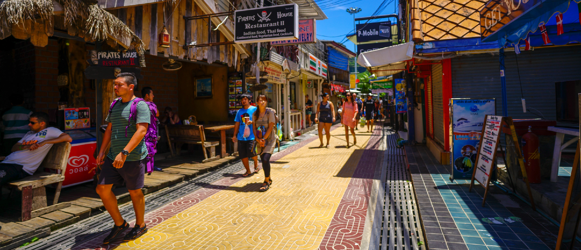 Tourists stroll along a vibrant, narrow street lined with shops and restaurants on Phi Phi Islands.