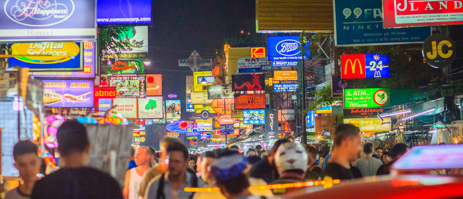 Crowds of people walk a vibrant street at night, illuminated by colorful neon signs in Bangkok.