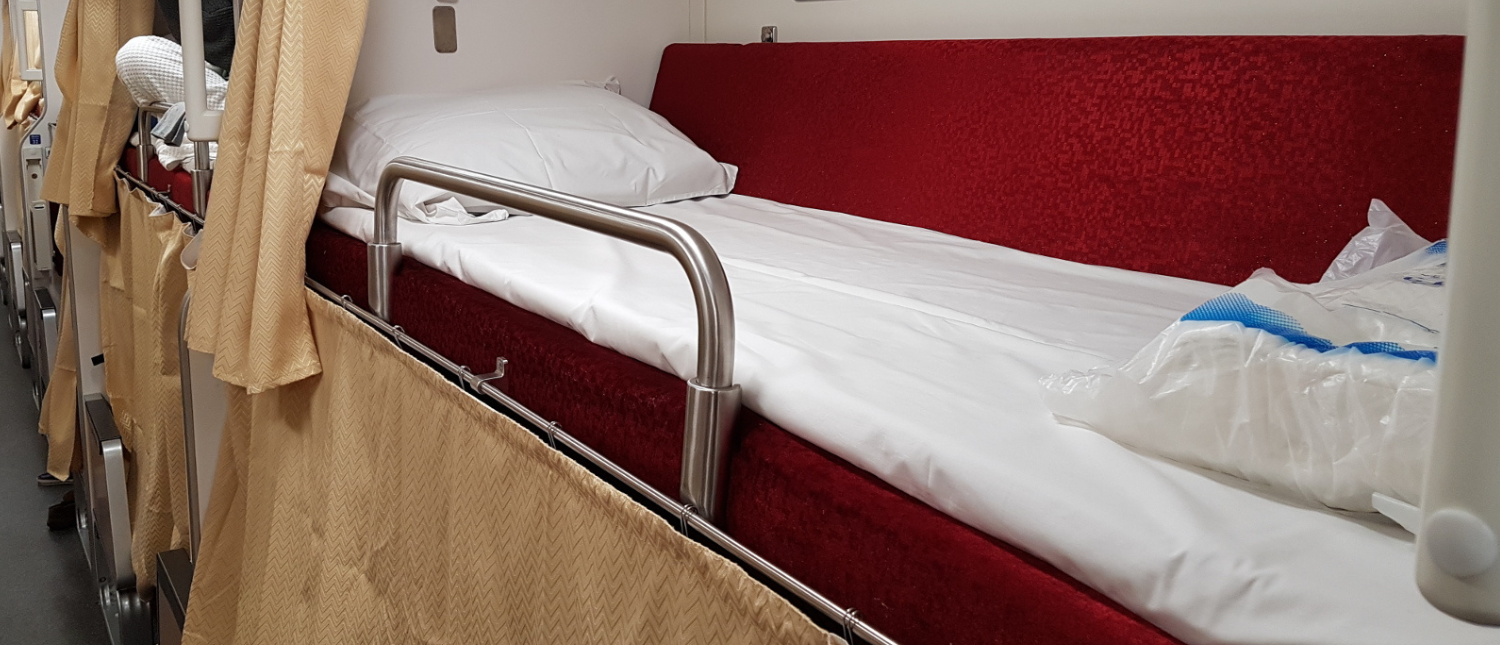 A comfortable sleeping bunk with privacy curtain on an overnight train journey through Thailand.