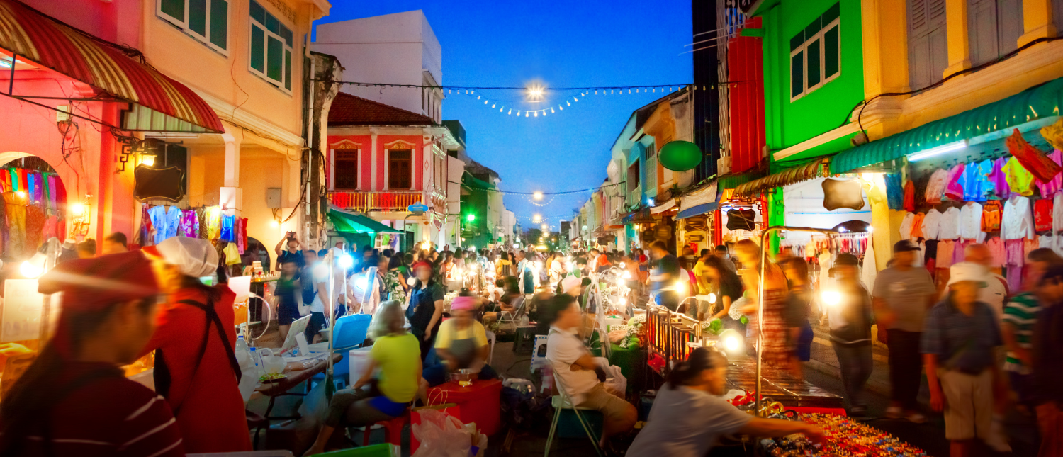 Shoppers explore a bustling night market in Phuket, filled with colorful stalls and historic architecture.