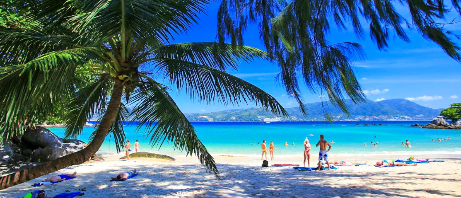 People relax on a beautiful Phuket beach with turquoise water and swaying palm trees.