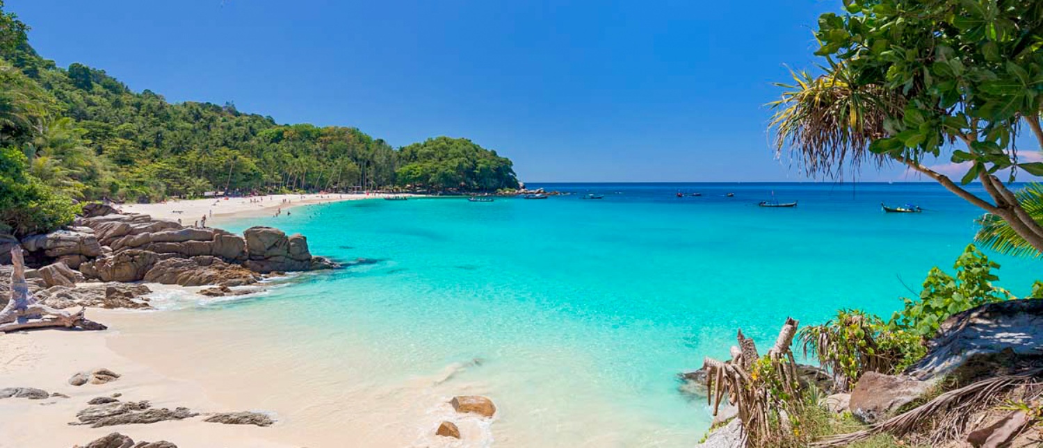 Idyllic Phuket beach with pristine white sand, calm turquoise sea, and verdant tropical foliage.