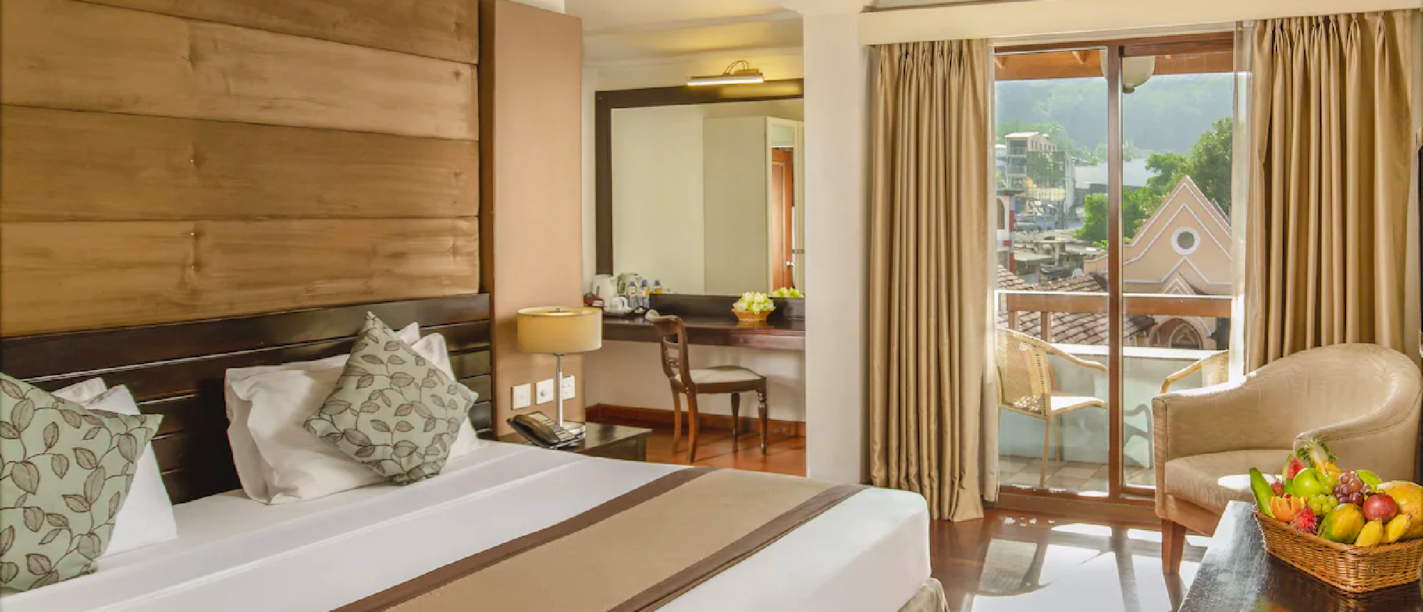 A comfortable hotel room in Kandy, Sri Lanka, with a bed, fruit basket, and balcony view.