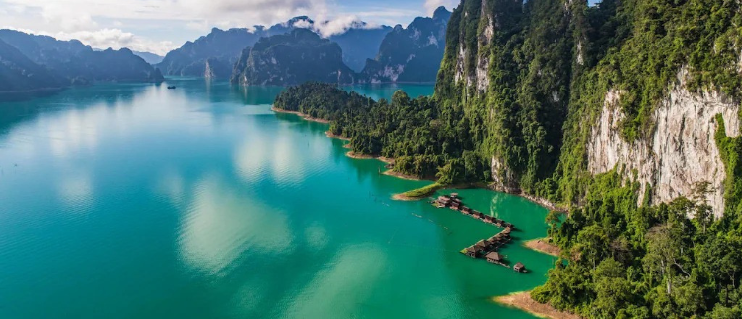 Majestic emerald lake surrounded by lush limestone cliffs and floating bungalows in Khao Sok National Park.