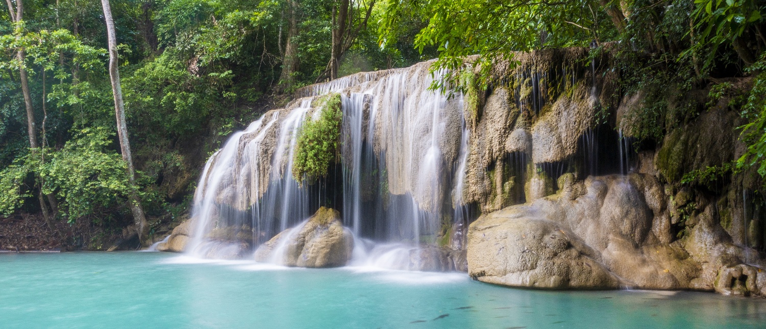 Beautiful Erawan Waterfalls cascade into a vibrant turquoise pool surrounded by lush green jungle in Thailand.