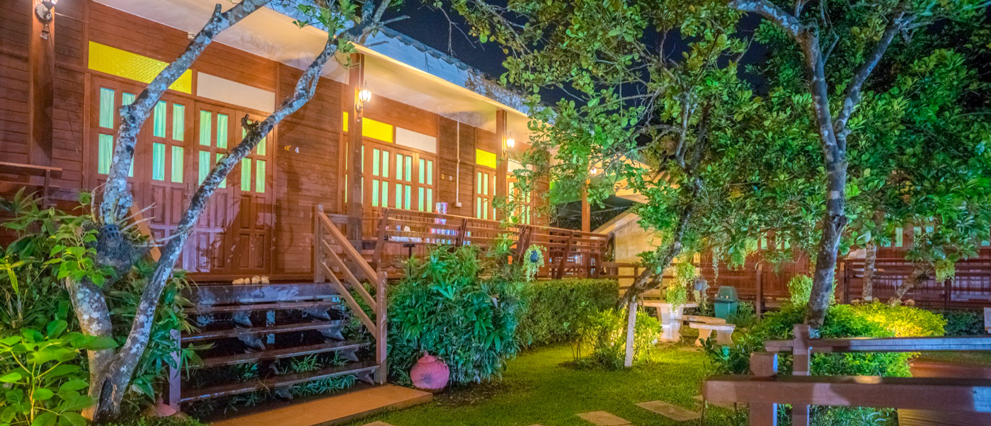 Charming traditional wooden homestay in Amphawa, Thailand, beautifully illuminated at night with a lush garden.