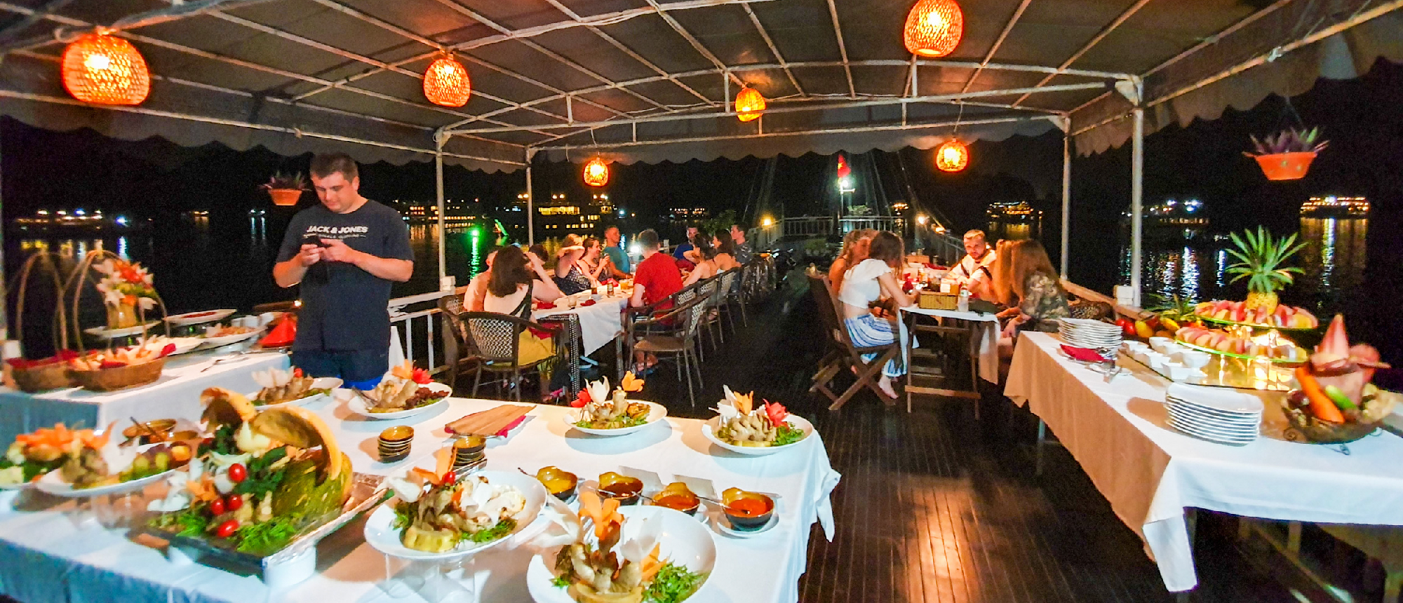 Guests enjoy a lavish buffet dinner on an illuminated cruise ship deck in Halong Bay.